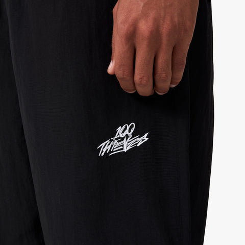 100 Thieves logo embroidered on left side of 100 Thieves Foundation nylon pants with elastic waistband and 100 Thieves metal aglet tipped drawstrings in the color black