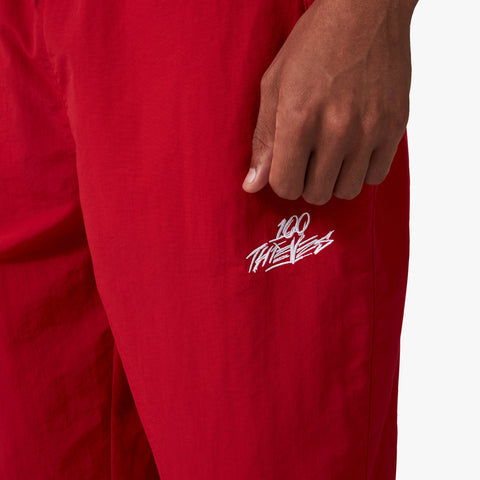 100 Thieves logo embroidered on left side of 100 Thieves Foundation nylon pants with elastic waistband and 100 Thieves metal aglet tipped drawstrings in the color red